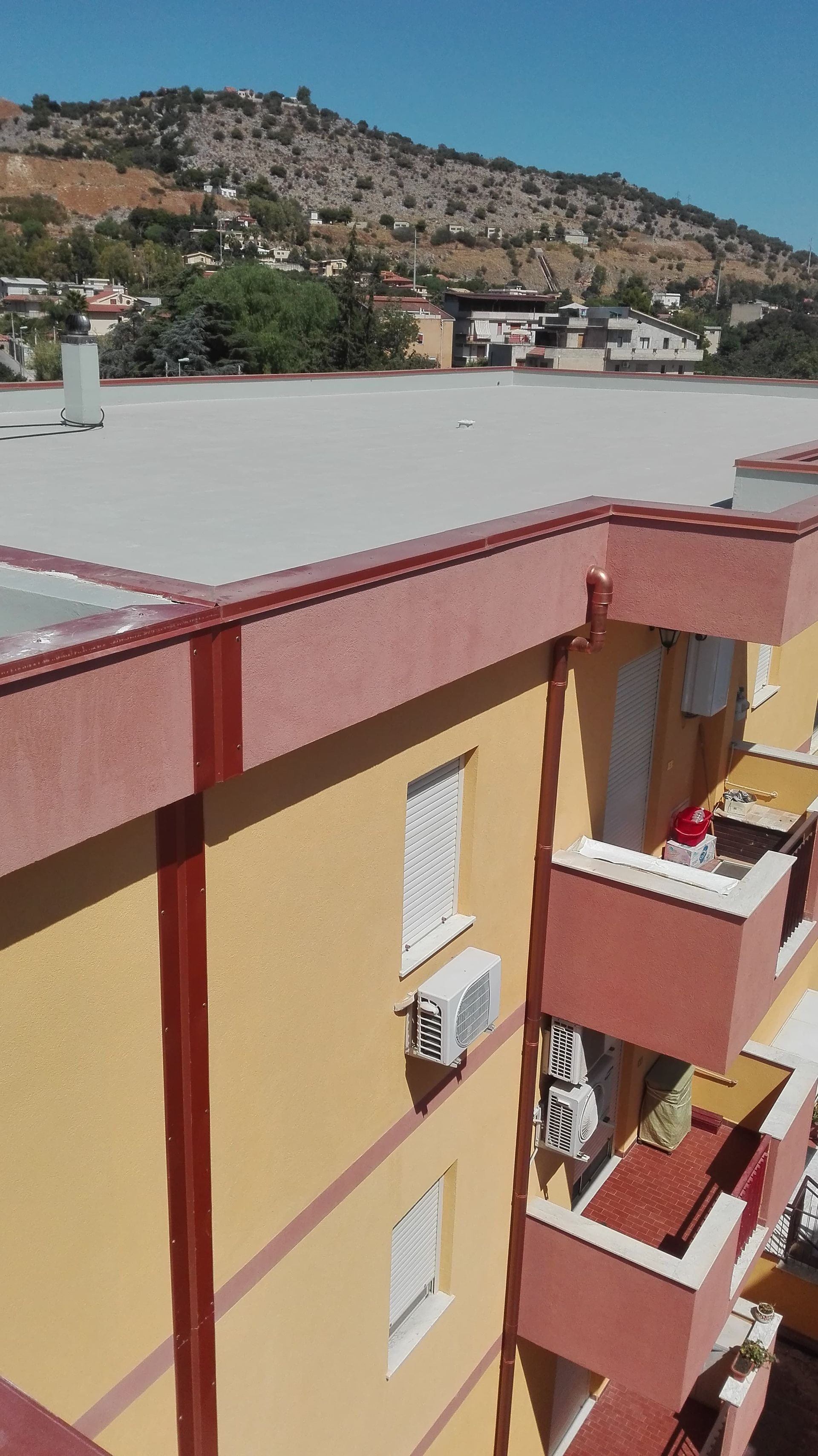 Edificio giallo con finiture e balconi rossi sullo sfondo di una collina.