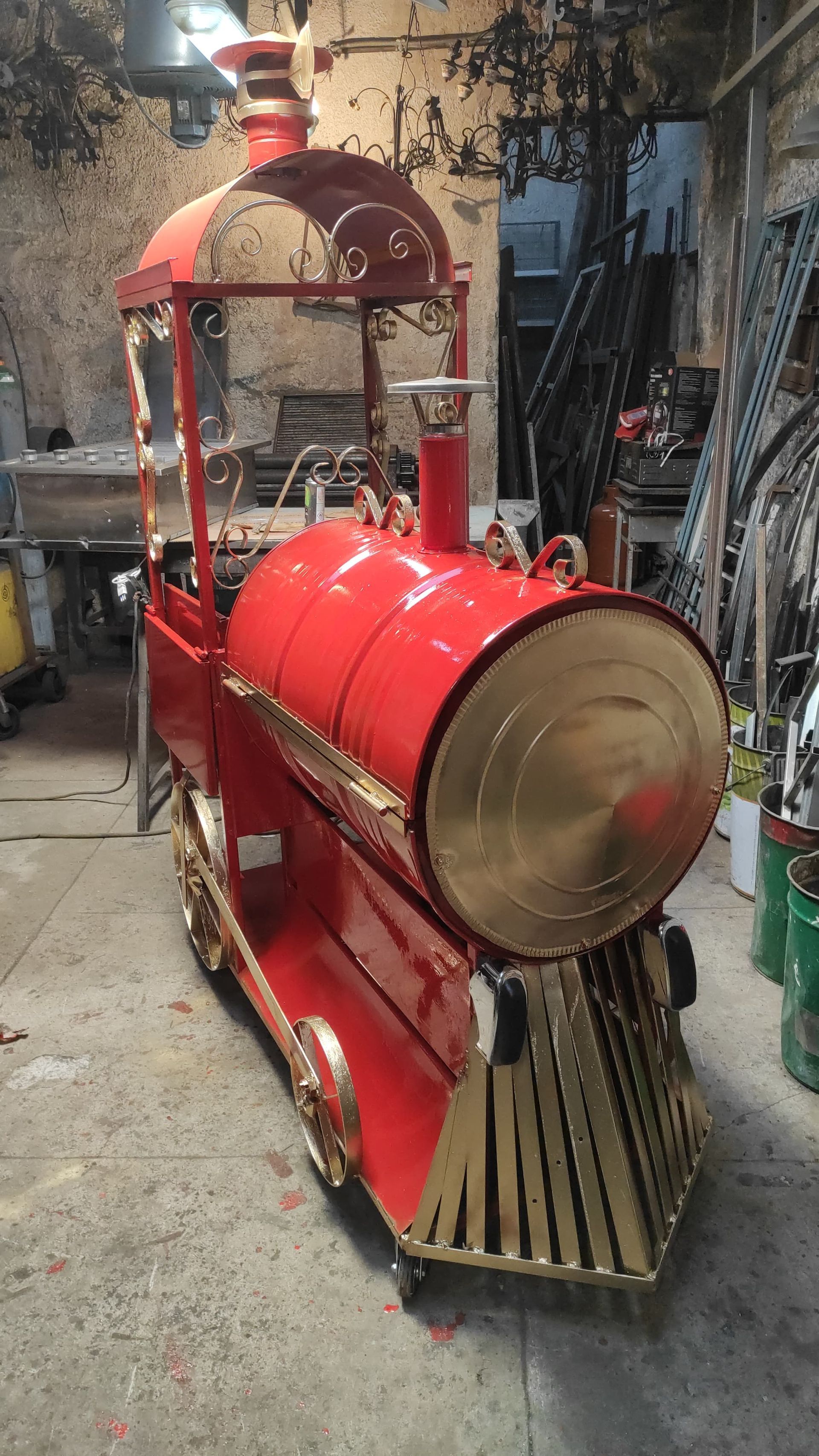 Treno decorativo rosso e oro con parte anteriore arrotondata e camino, probabilmente destinato a un parco o a un evento.