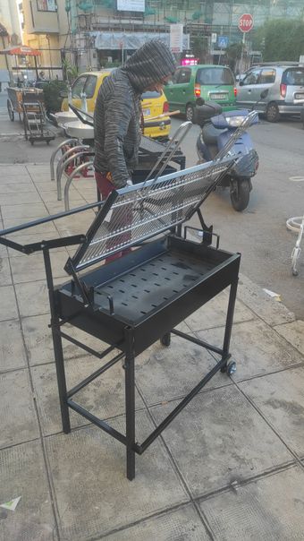 Griglia per barbecue in metallo nero su un marciapiede. Persona vicino. Auto ed edifici sullo sfondo.