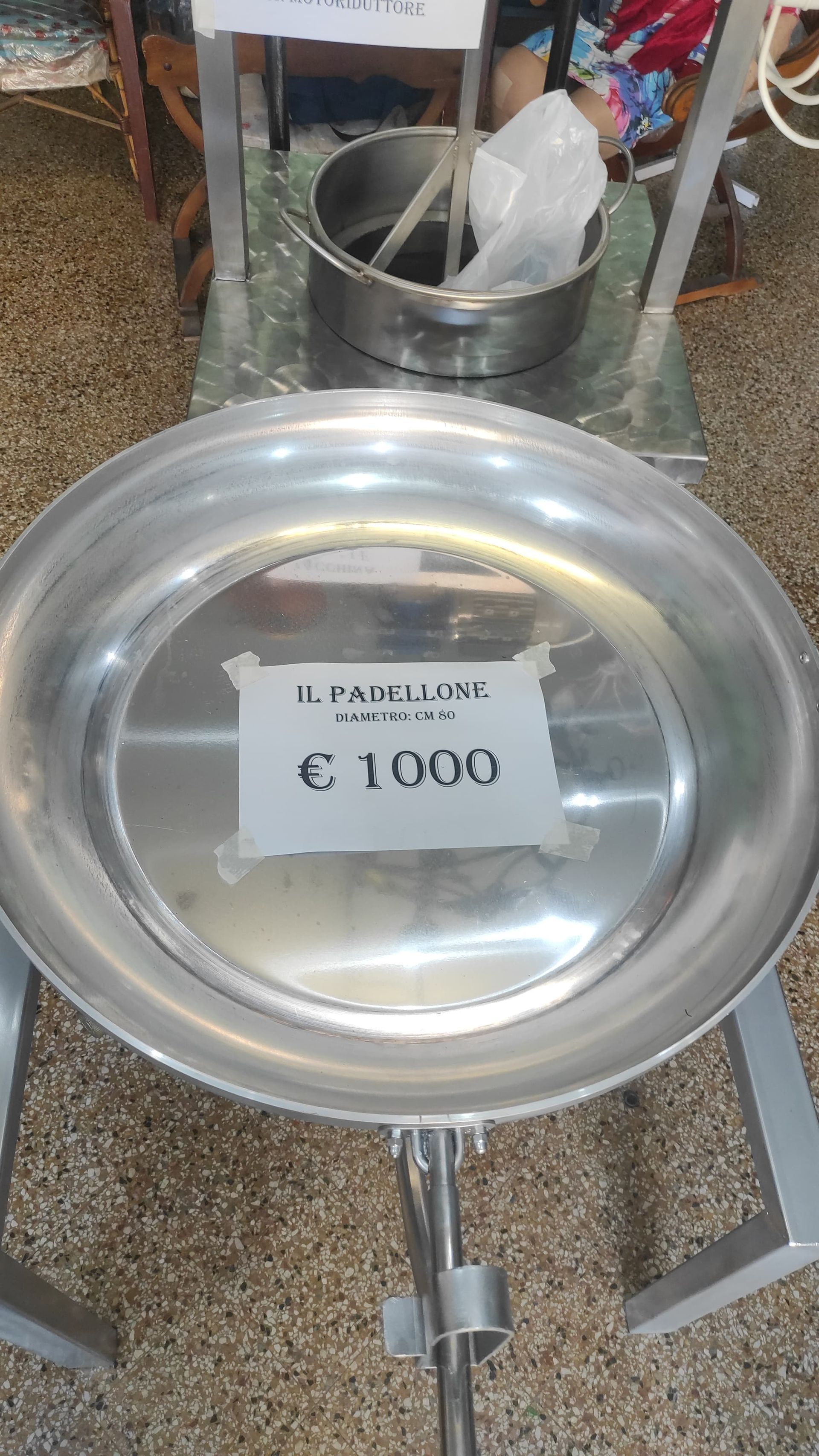Grande padella di metallo su una bilancia con un cartellino del prezzo di 1000 €.