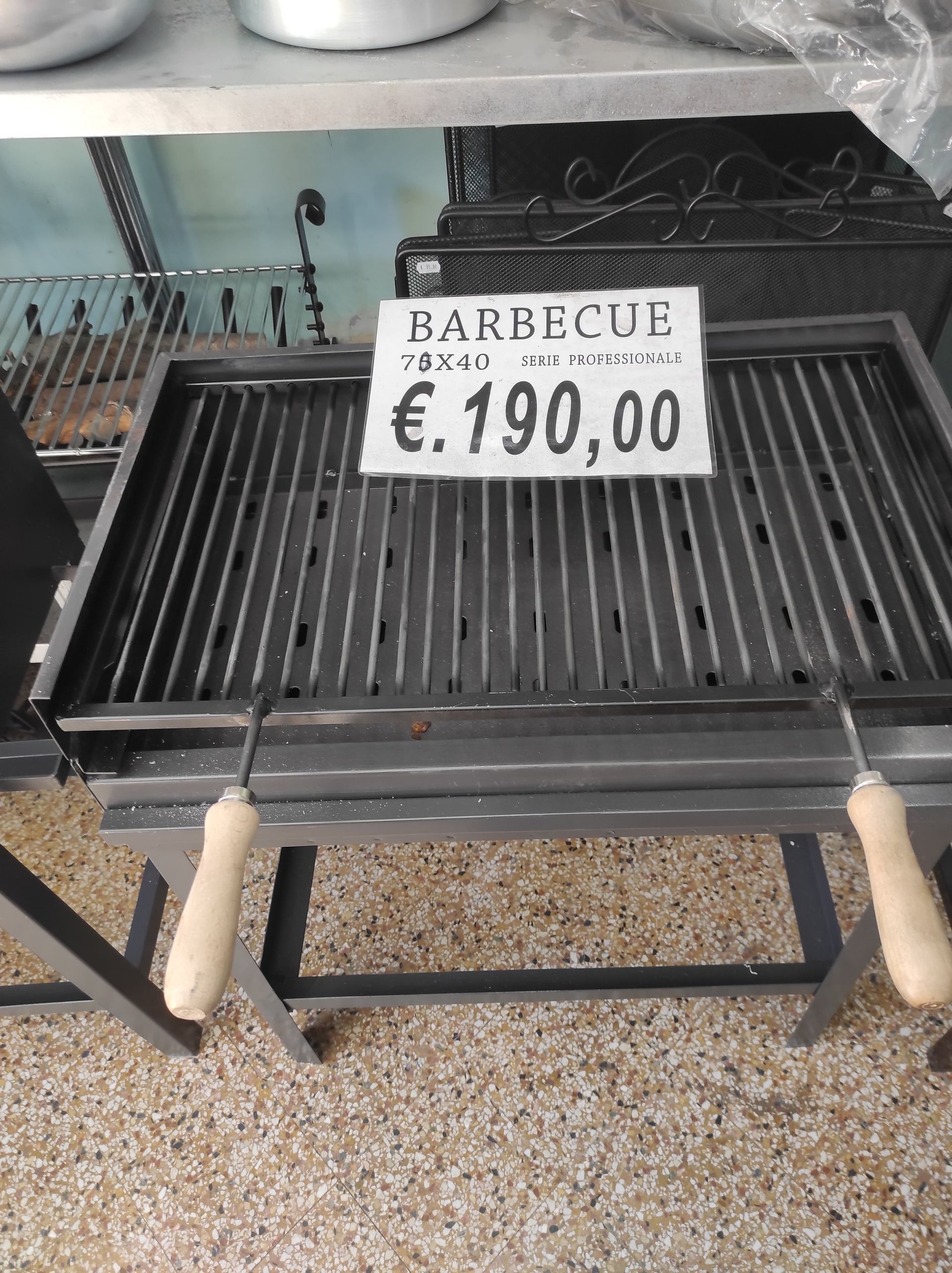 Barbecue in metallo con cartellino del prezzo. Griglia nera, manici in legno, su supporto grigio. € 190,00