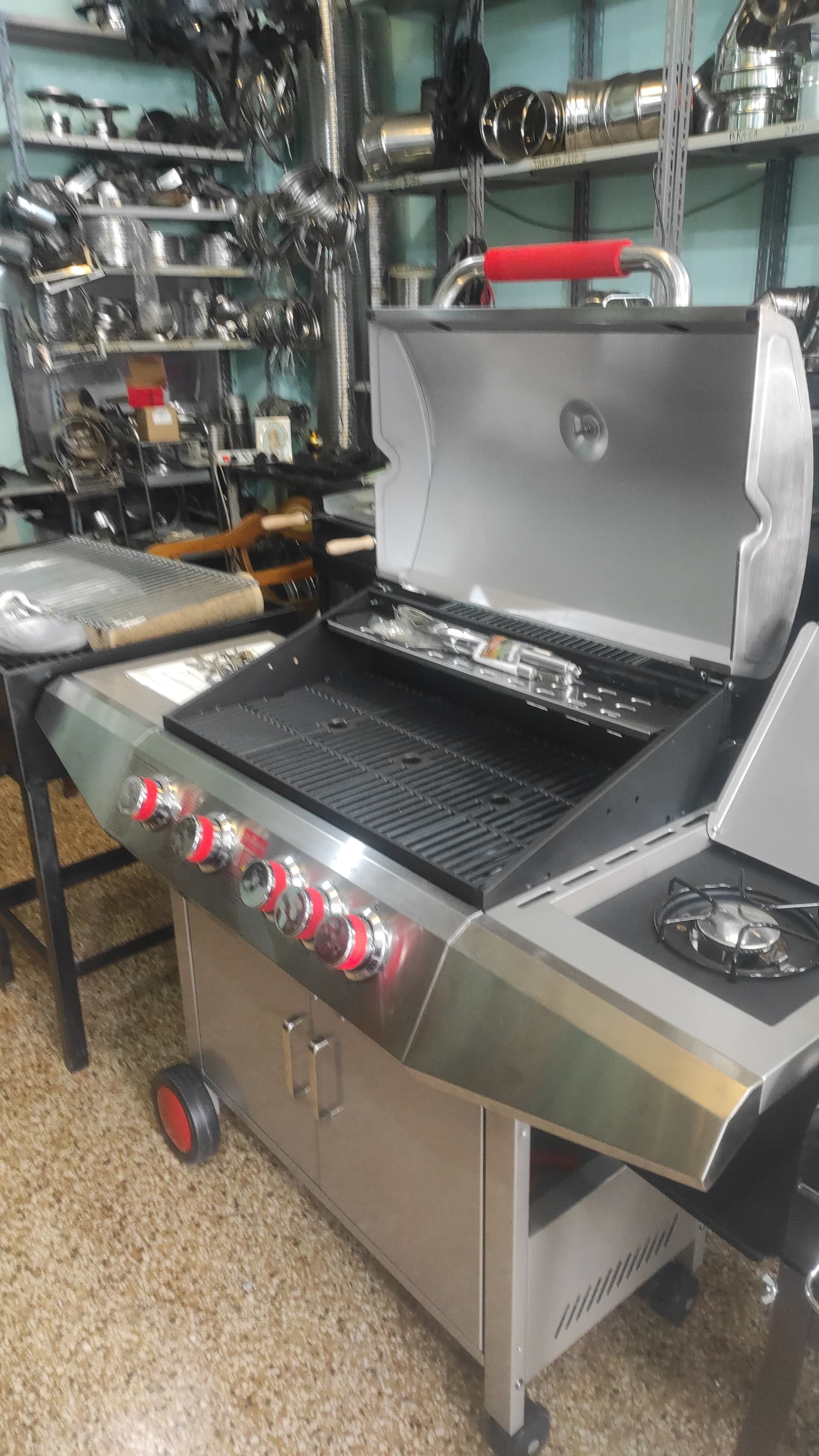 Una griglia a gas in acciaio inossidabile con manopole rosse e superficie di cottura nera, in un negozio.