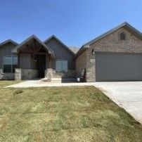 A large brick house with a gray garage door and a large lawn in front of it.