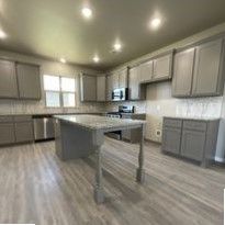A kitchen with gray cabinets , stainless steel appliances , and a large island.