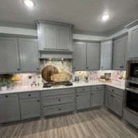 A kitchen with gray cabinets , white counter tops , and stainless steel appliances.