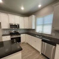 A kitchen with white cabinets , black counter tops , stainless steel appliances , and a sink.