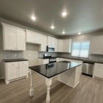 A kitchen with white cabinets , black counter tops , stainless steel appliances and a large island.