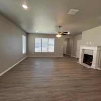 An empty living room with a fireplace and ceiling fan.