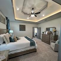 A bedroom with a bed , dresser , chair and ceiling fan.