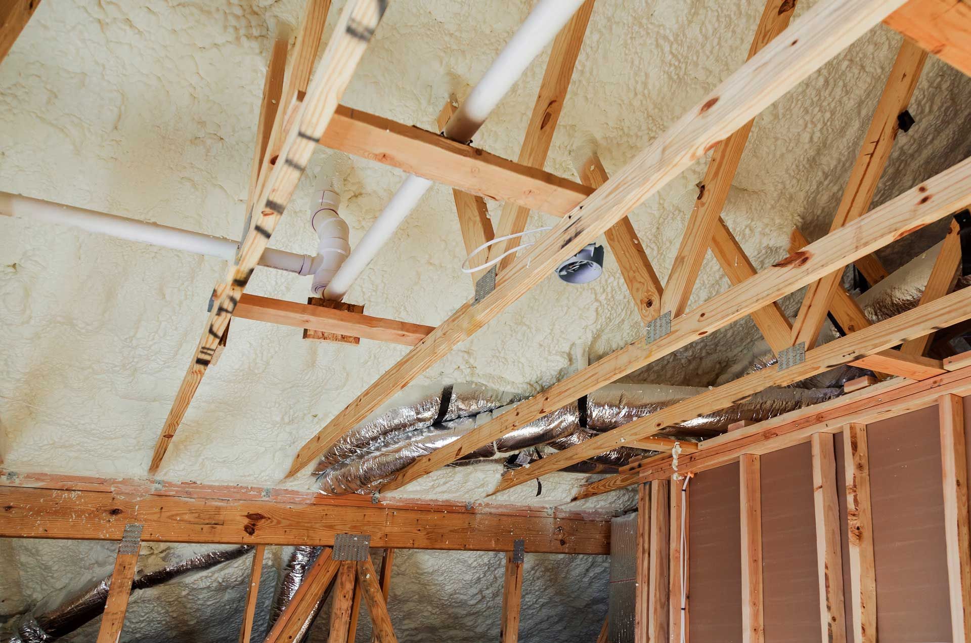 Wooden rafters and pipes inside a building under construction, sprayed with insulating foam.
