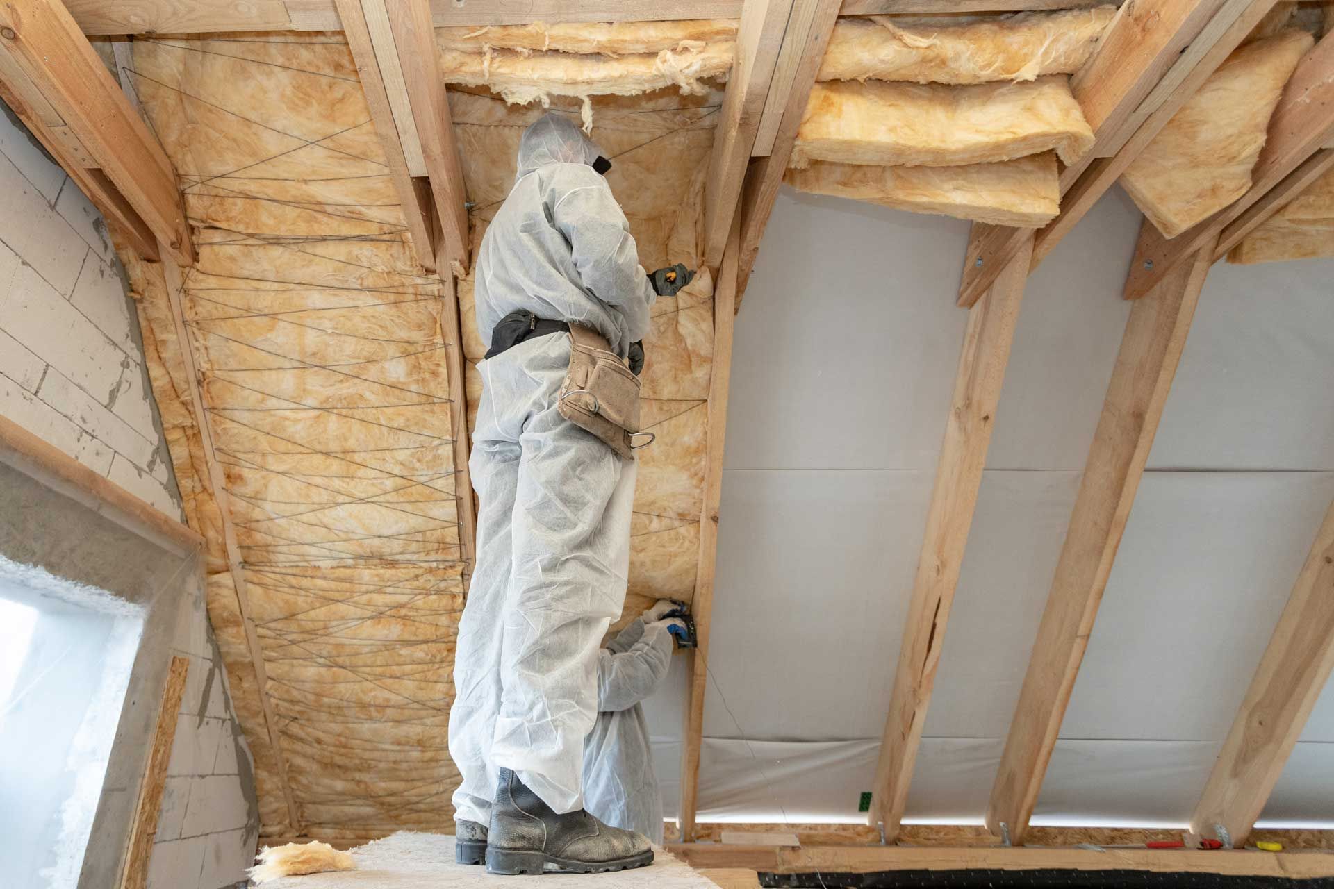 Workers in protective suits installing insulation in an attic.