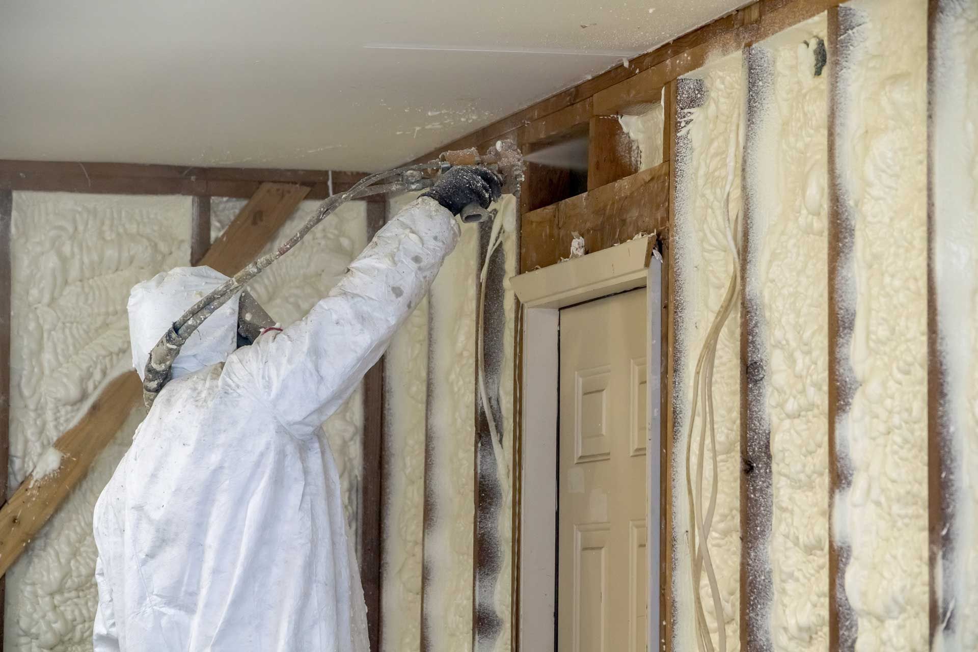 Person in protective suit spraying insulation foam on interior wall.