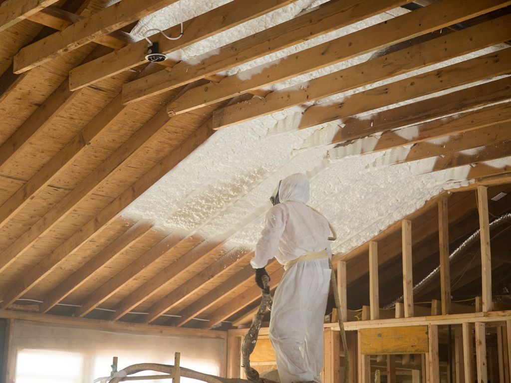 Person in protective suit spraying foam insulation in an attic.