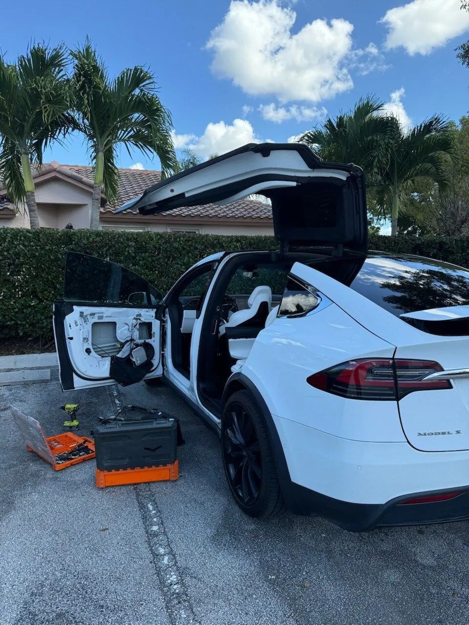 White Tesla with open doors and tools nearby, parked outside, sunny day.