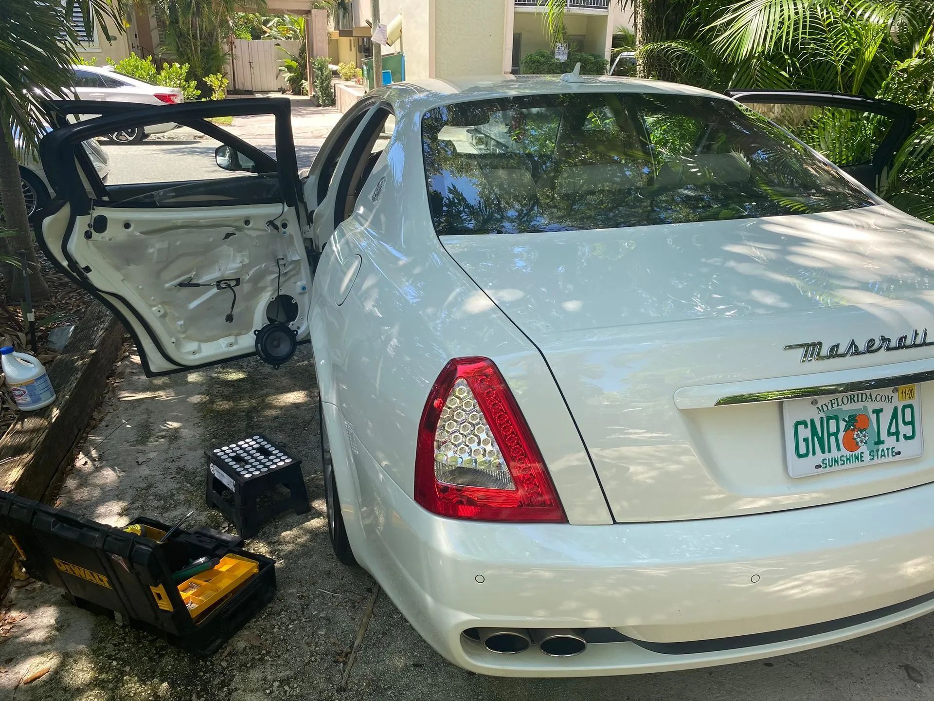White Maserati with open doors, tools nearby, Florida license plate, being worked on outdoors.