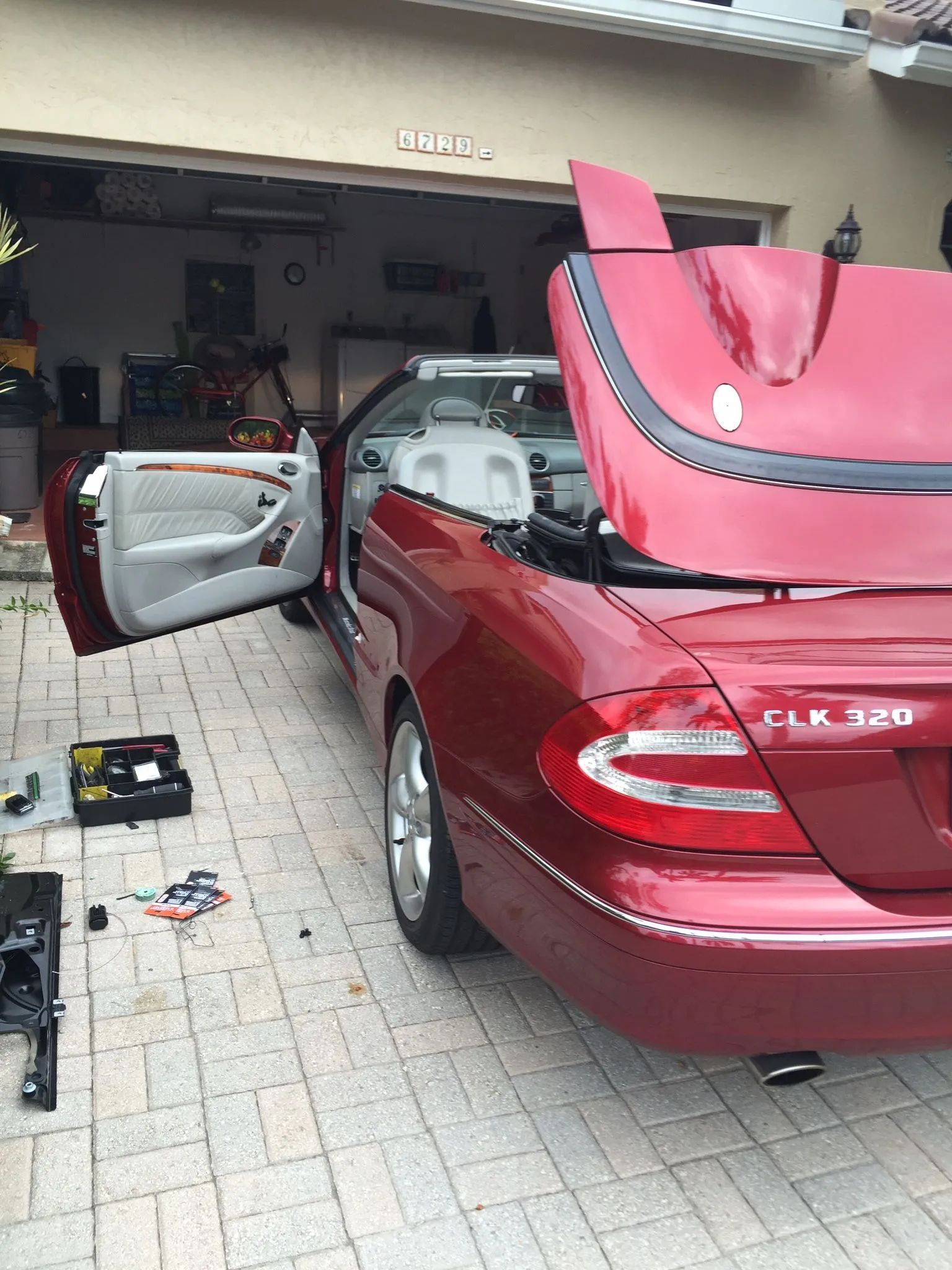 Red Mercedes sedan in a garage with the hood open and driver door ajar
