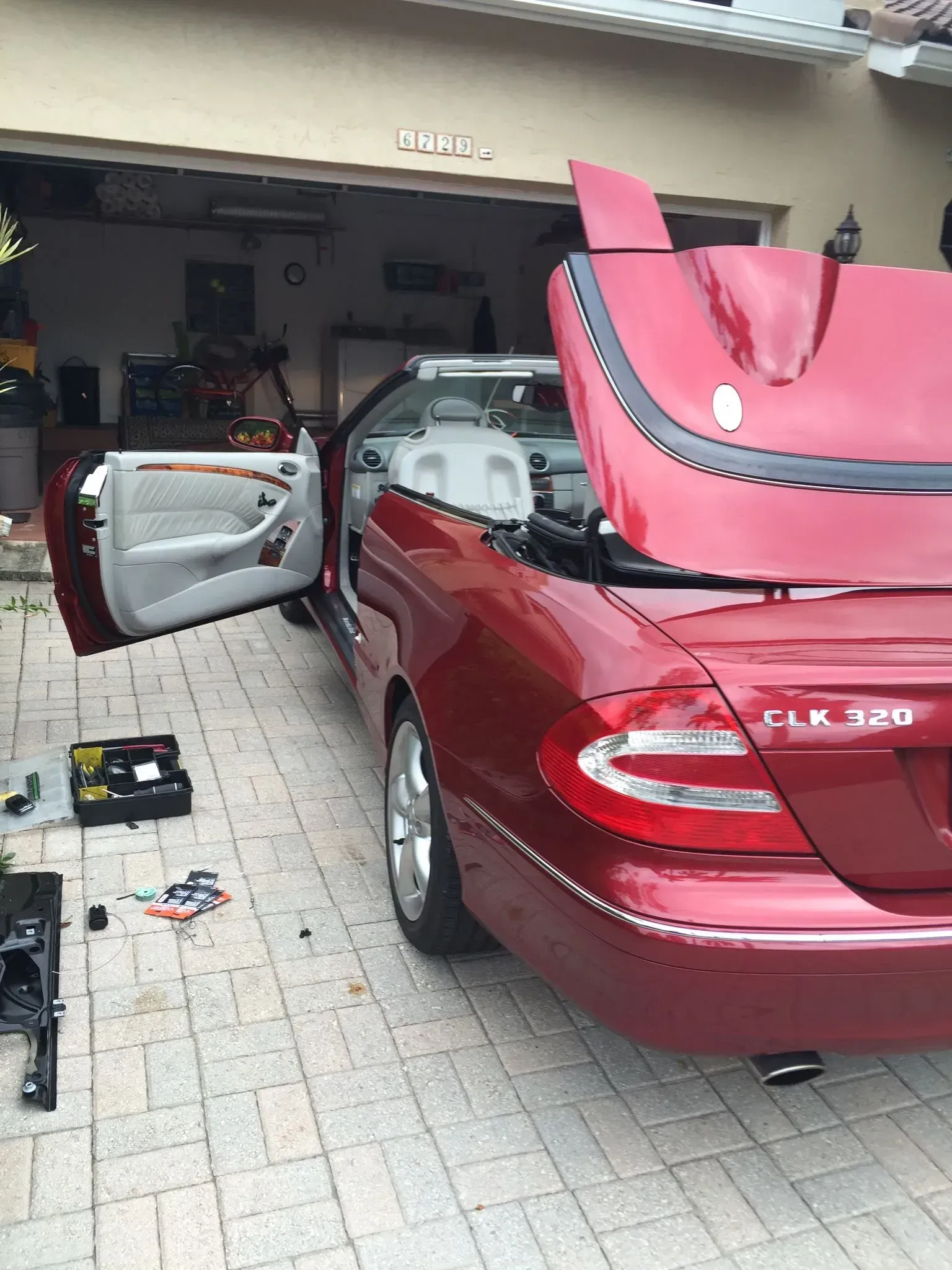 A red convertible with the hood up is parked in a garage.