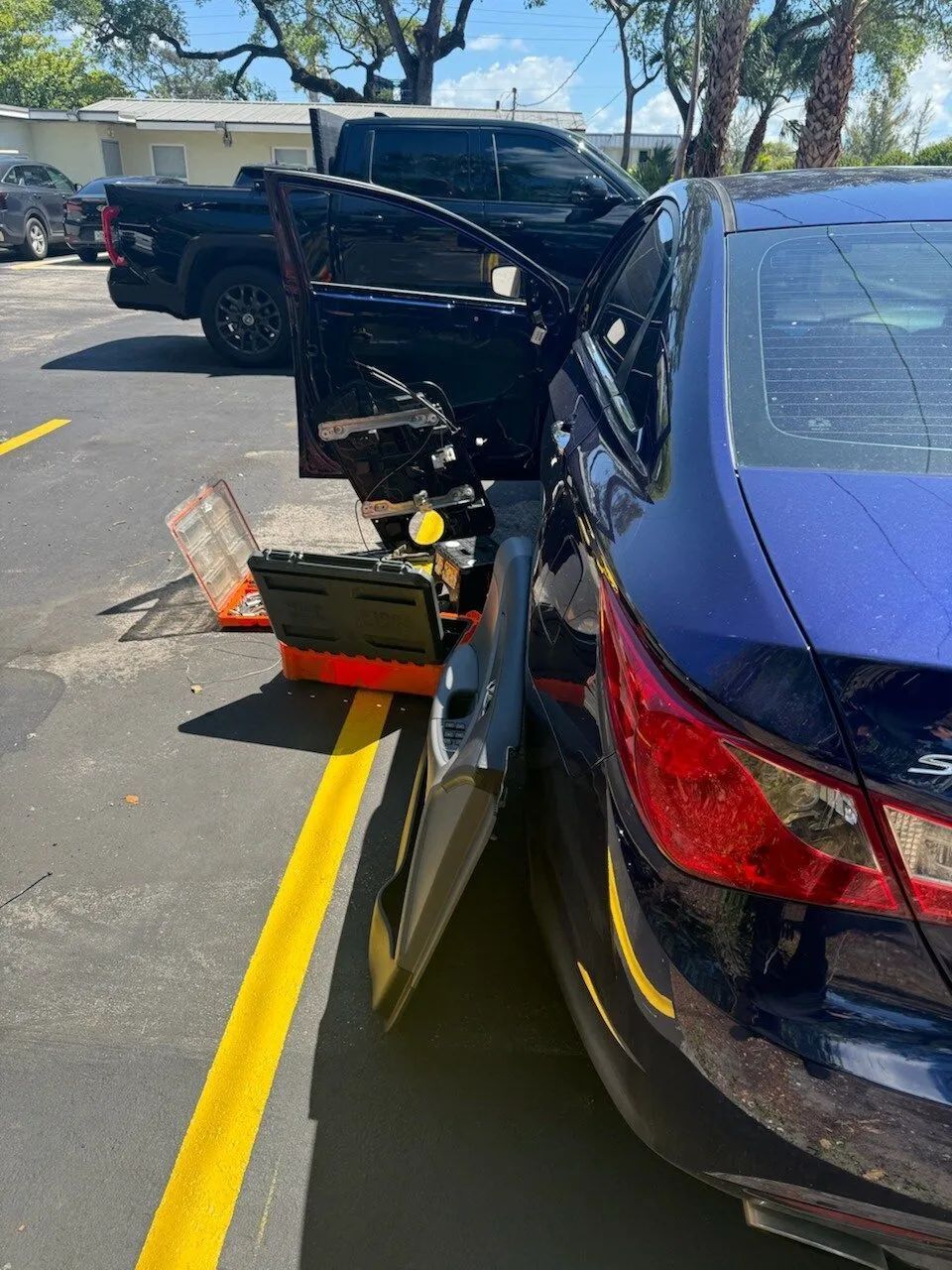 A dark blue car with its rear driver-side door panel removed, parked in a lot next to a black pickup truck.