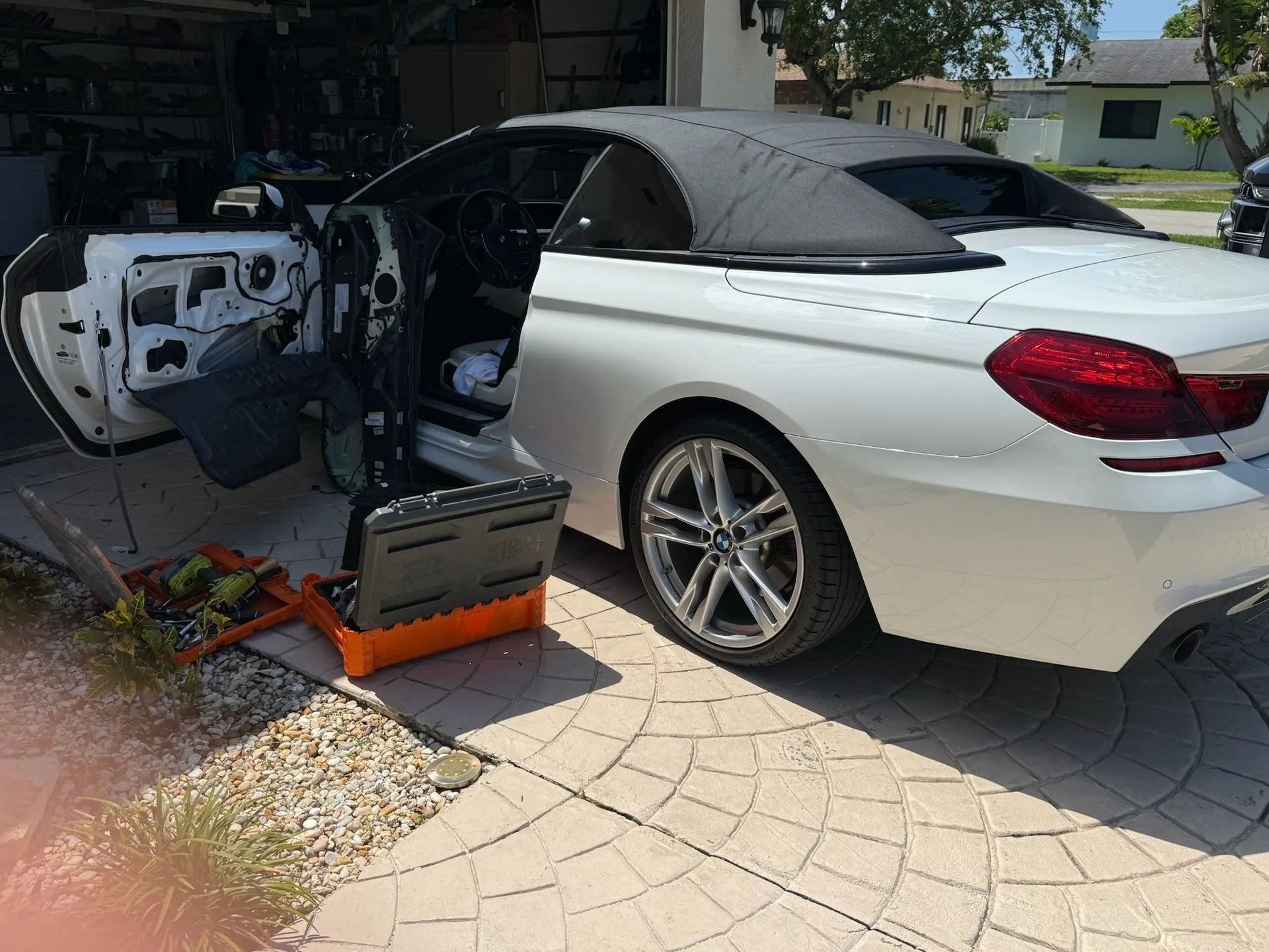 A white convertible with its driver-side door panel removed, parked in a driveway next to an open toolbox.