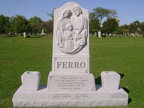 Gray Ferro family gravestone with carved family scene, two vase holders, and text in a cemetery.