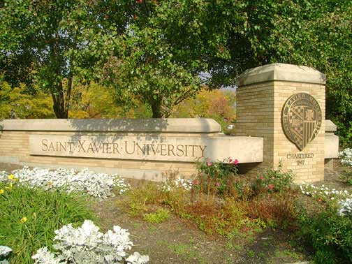 Saint Xavier University sign in front of foliage and flowers.