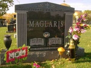 Headstone of the Maglaris family with flower arrangements in a cemetery.
