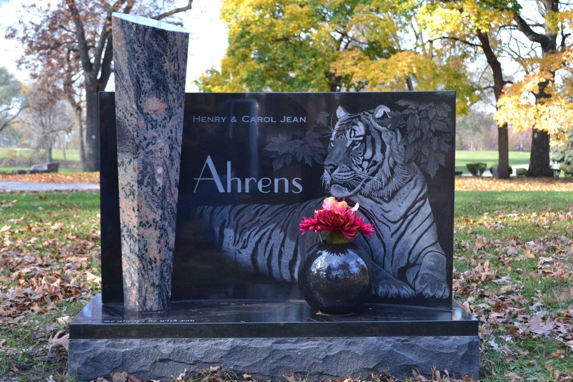 Black granite tombstone with tiger engraving, flowers, and the name 