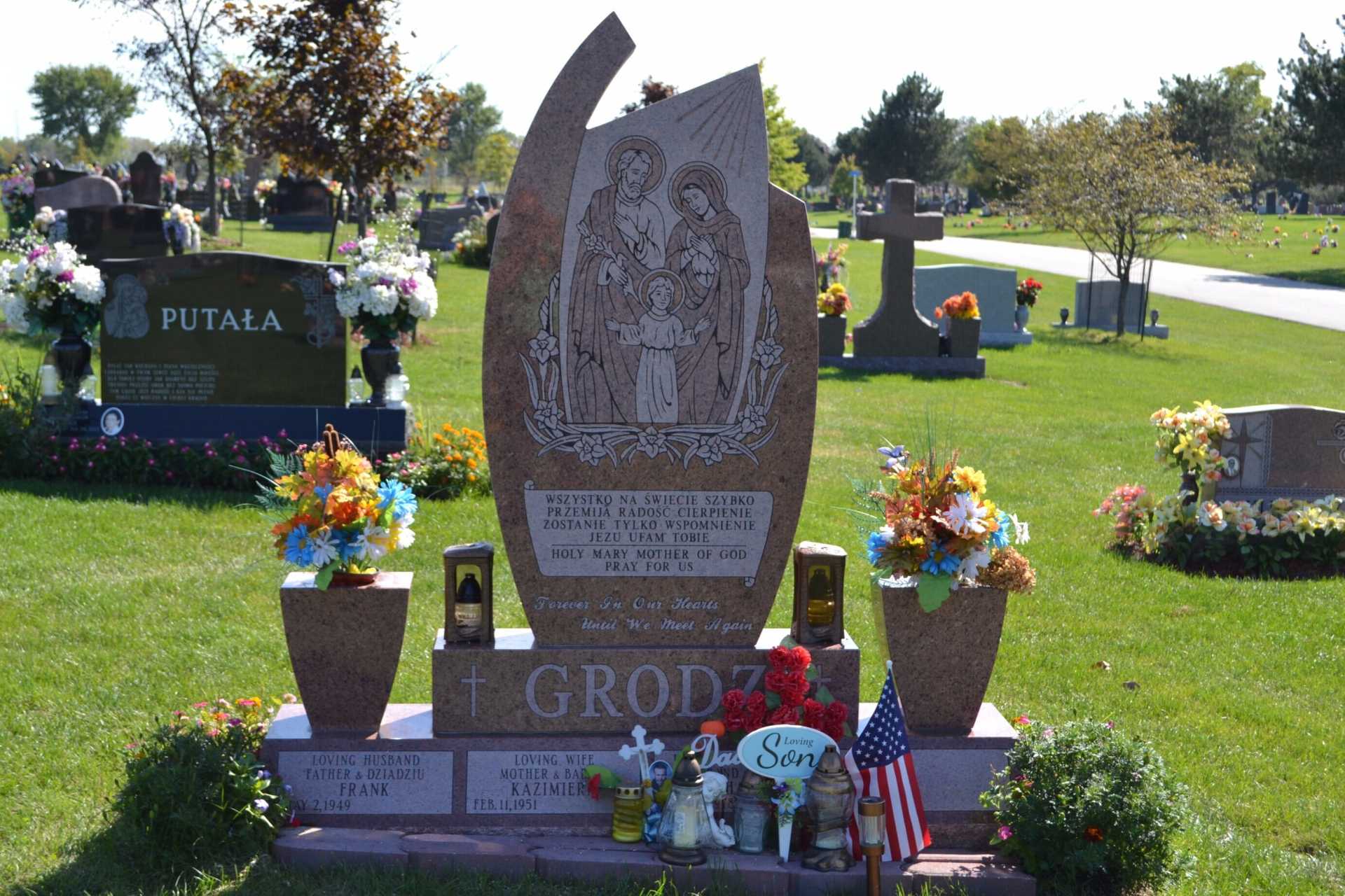 Grave site with floral arrangements, statues, and flags in a cemetery.
