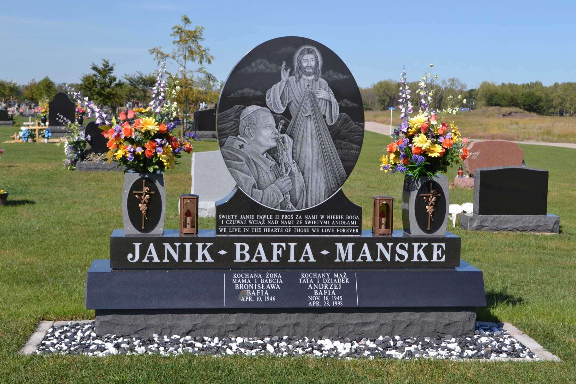 Headstone in cemetery with floral arrangements and engraved religious figures.