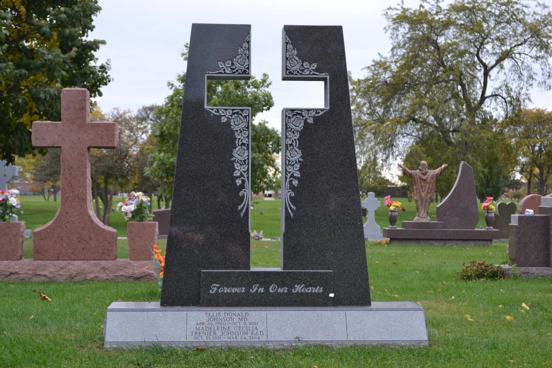Black granite monument with a cross-shaped cutout, floral details, and inscription in a cemetery.