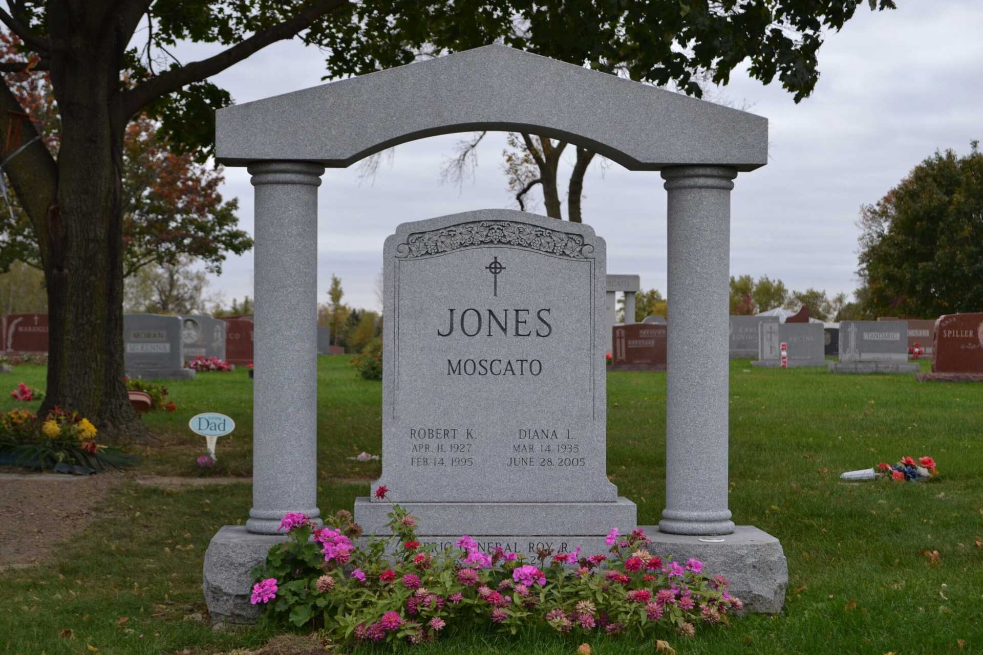 Gray gravestone in a cemetery with a decorative arch, the name 