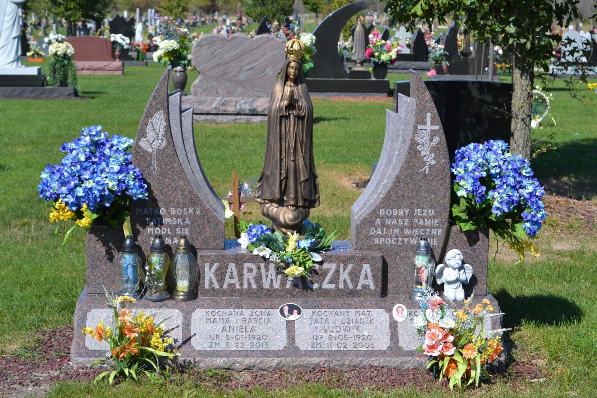 Grave marker with statue of a saint, flowers, and the name 