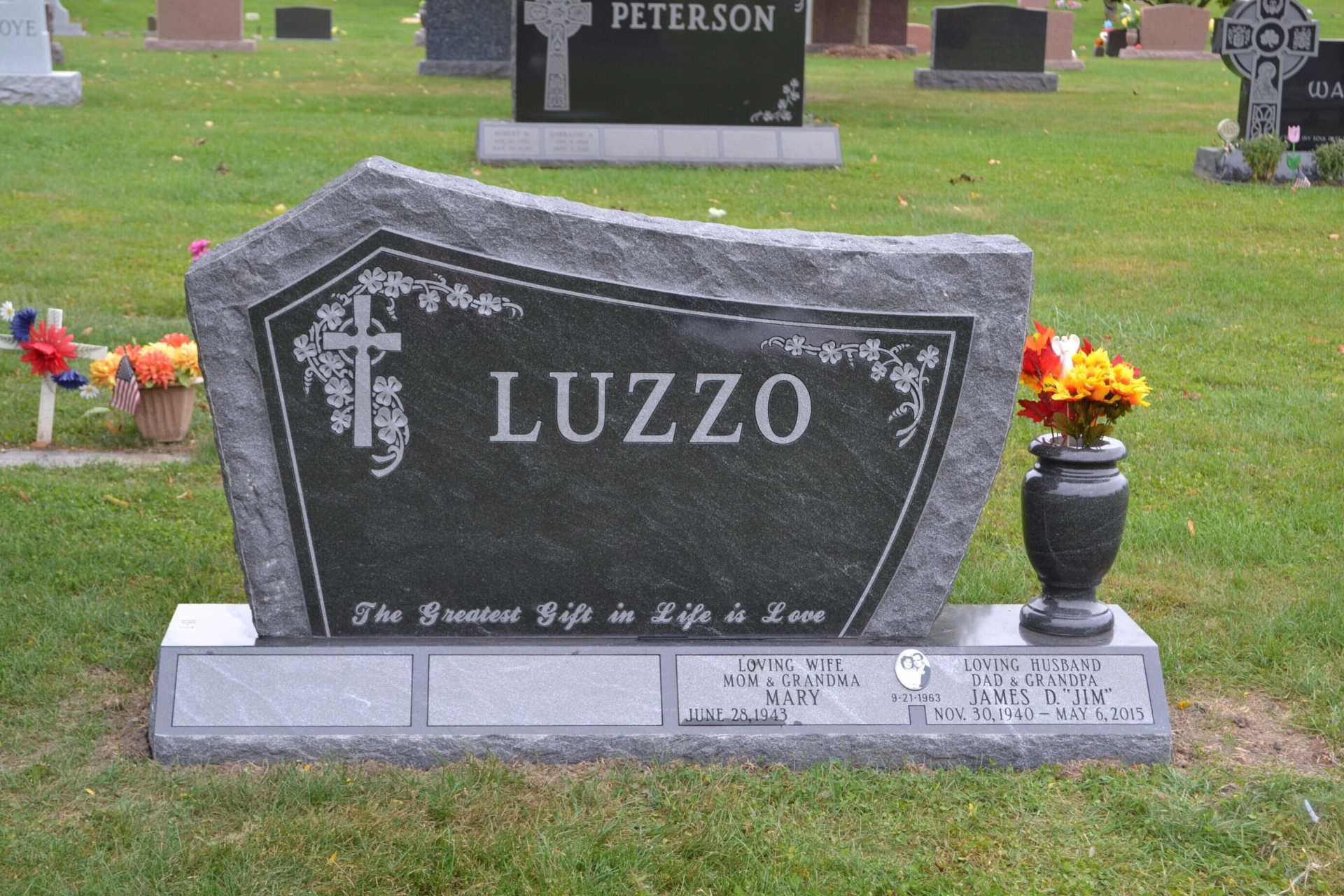 Headstone for LUZZO with floral design, cross, and epitaph in a cemetery.