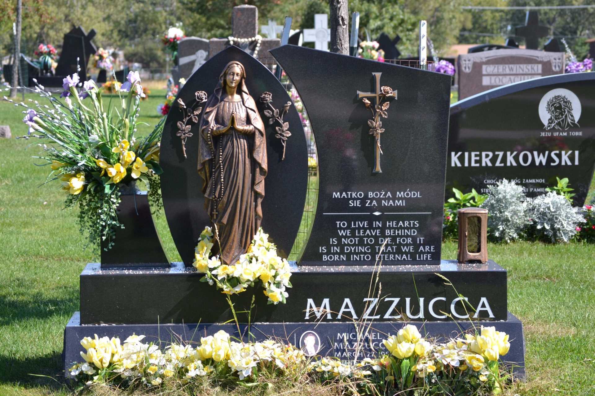 Headstone with statue of a woman, flowers. 