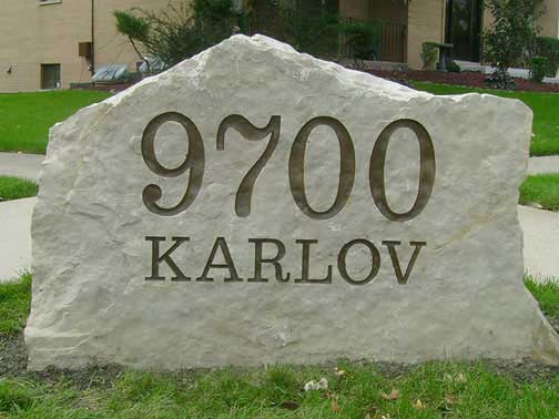 Stone sign: 9700 Karlov carved into a large, light-colored rock, set in grass.