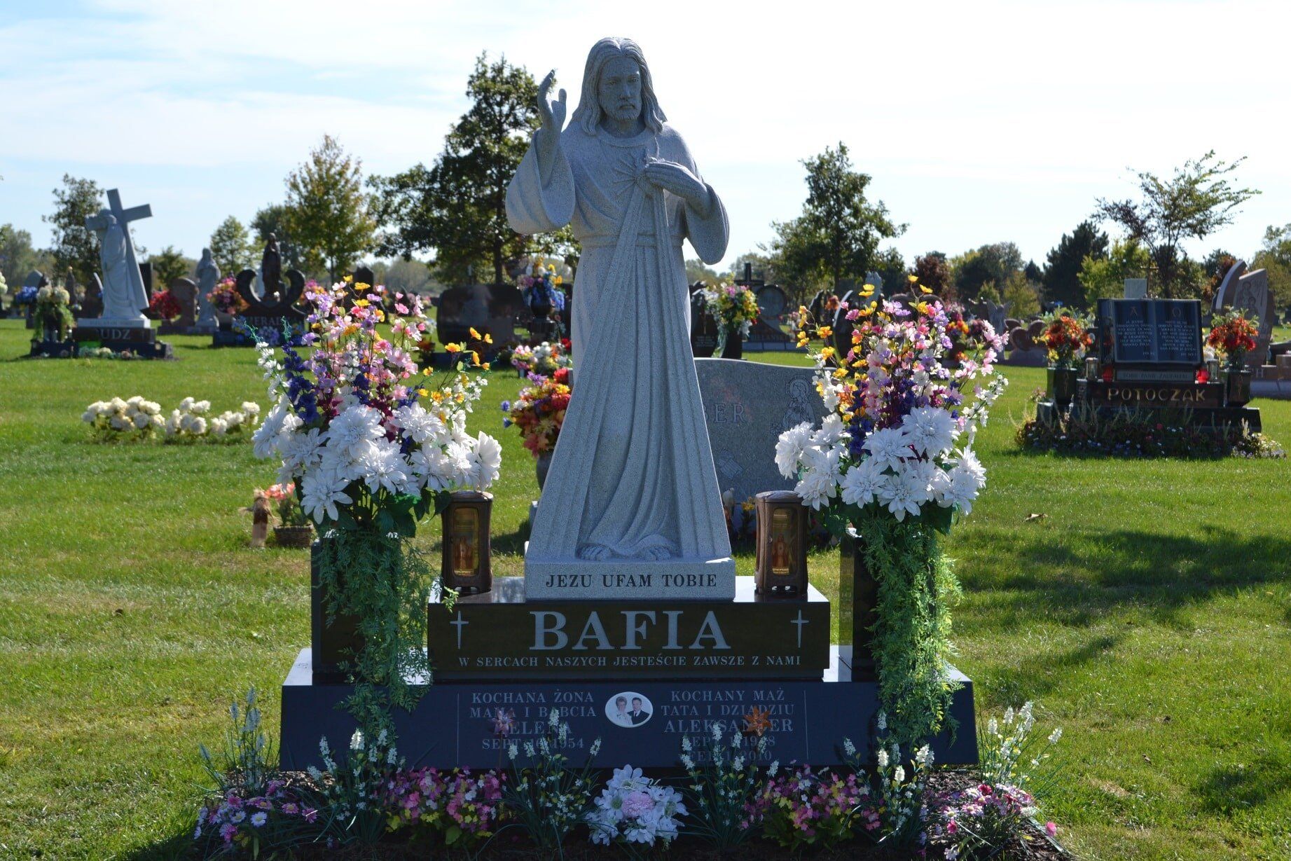 Statue of Jesus on a headstone in a cemetery, surrounded by flowers.