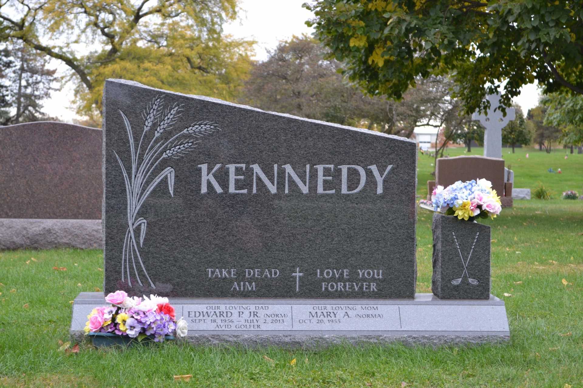 Kennedy family gravestone with floral arrangements in a cemetery. Gray stone, inscription 
