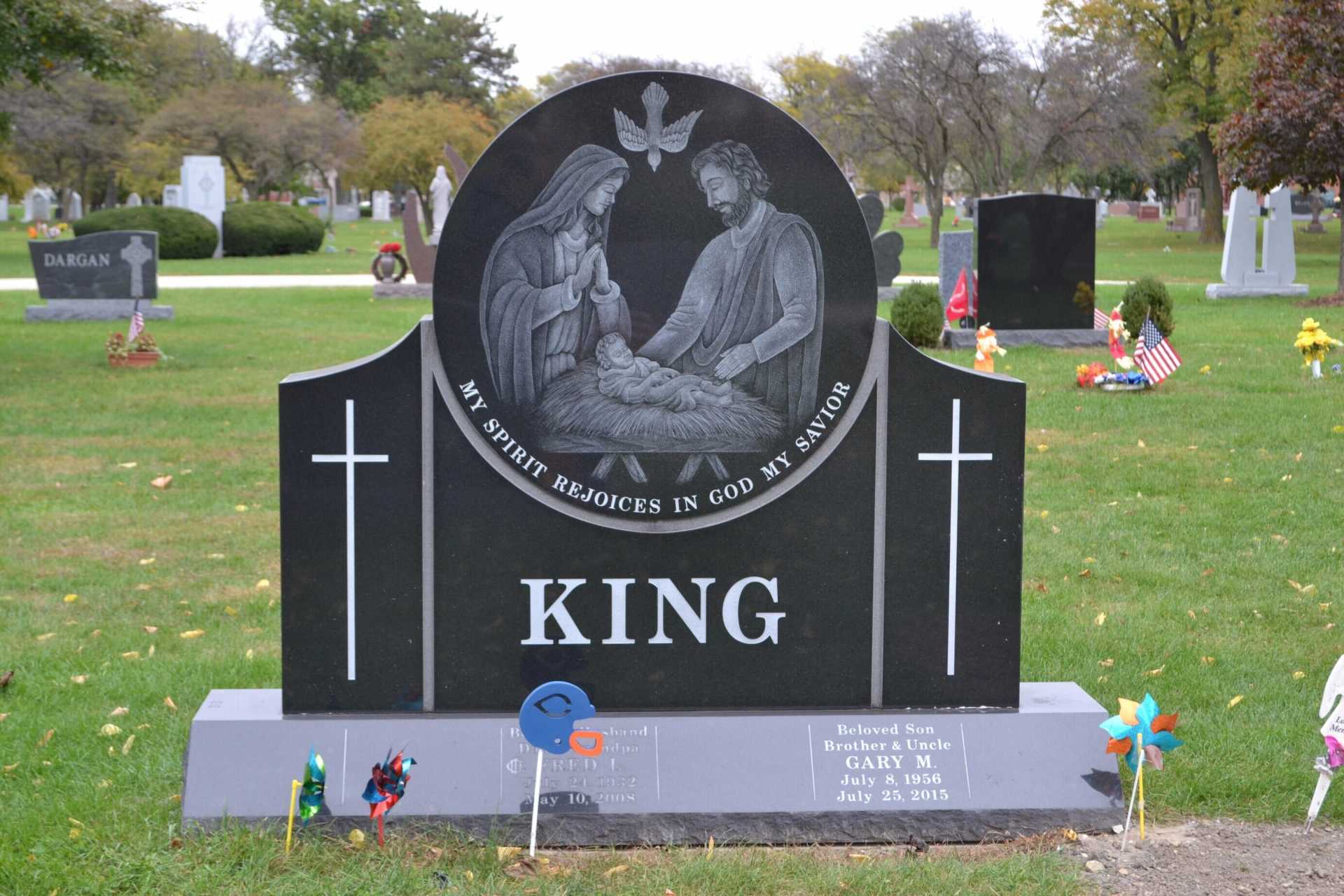 Black headstone with religious scene; KING name; cemetery setting.