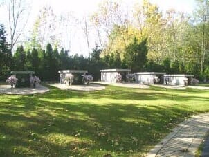 Grave markers in a green grassy area, some with flowers; trees in the background.