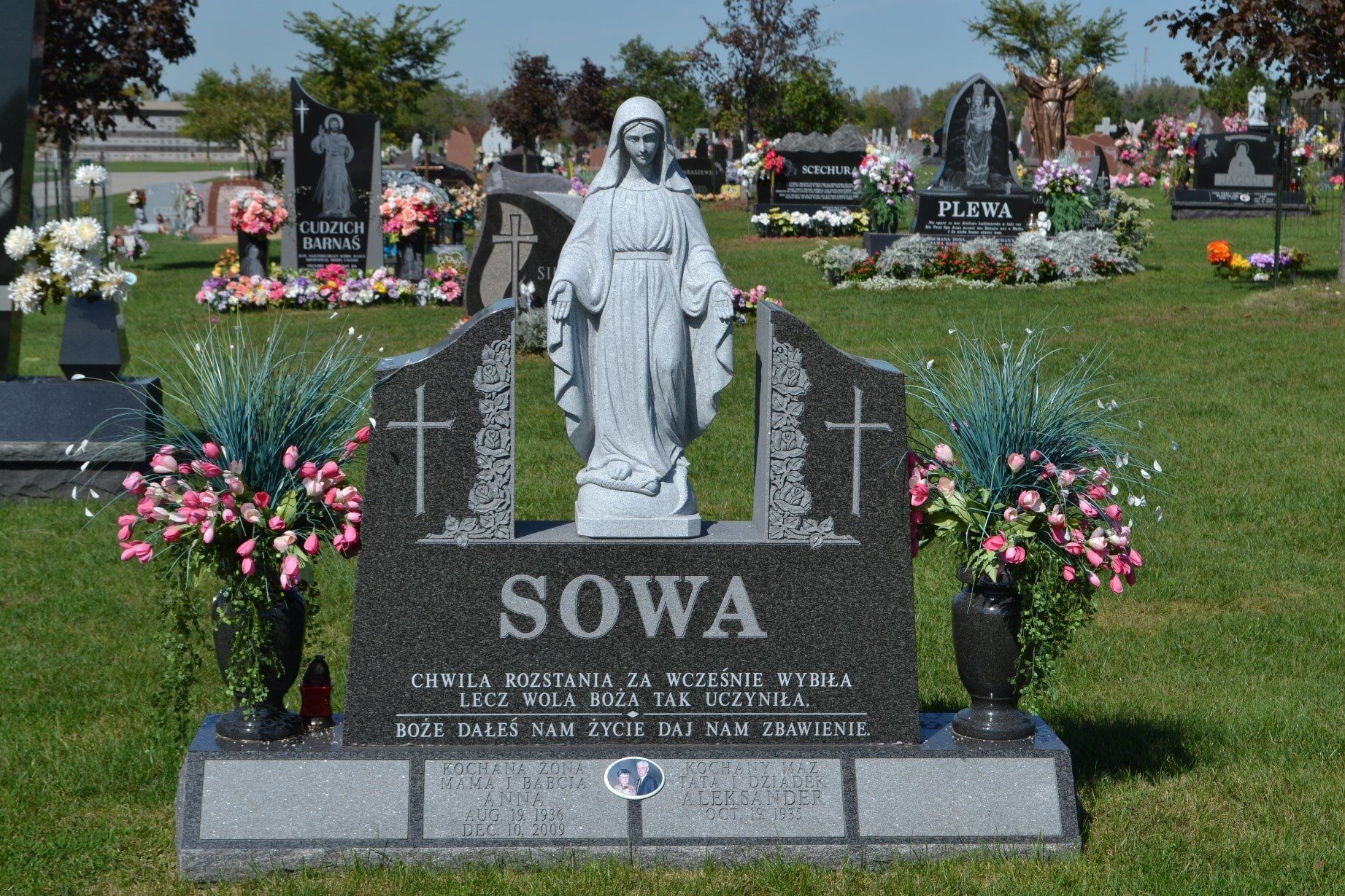 Granite tombstone with statue of a woman, flowers in a cemetery.