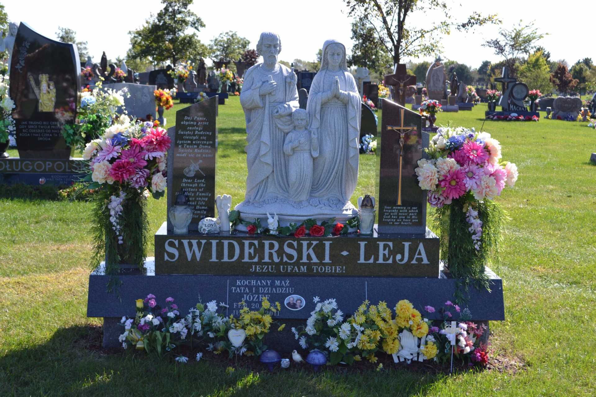 Headstone with family statue, flowers, and names SWIDERSKI - LEJA in a sunny cemetery.