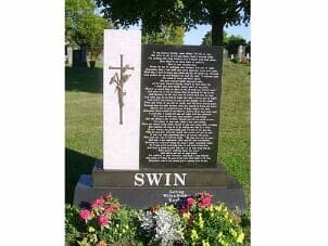 A tombstone in a cemetery, featuring a cross, text, and flowers at the base.