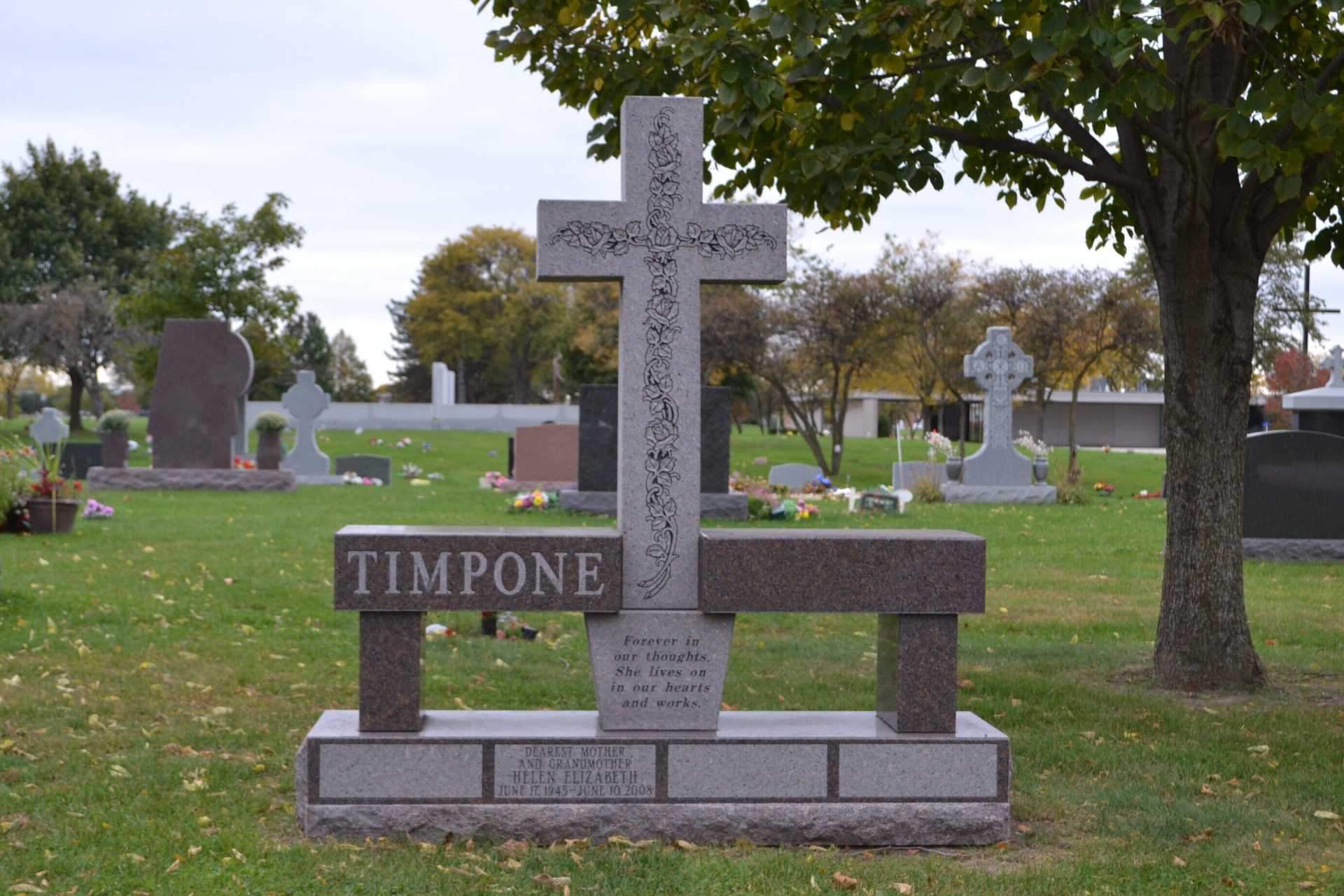 Headstone at a cemetery with a cross, bench, and the name TIMPONE.