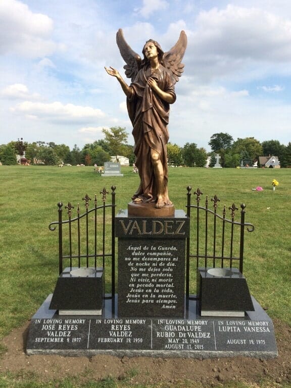 Bronze angel statue on a tombstone in a cemetery. The tombstone has the name 