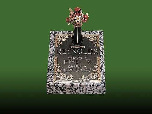 Grave marker with a bronze plaque, floral design, and vase of flowers. Name: Reynolds. Granite base, green background.