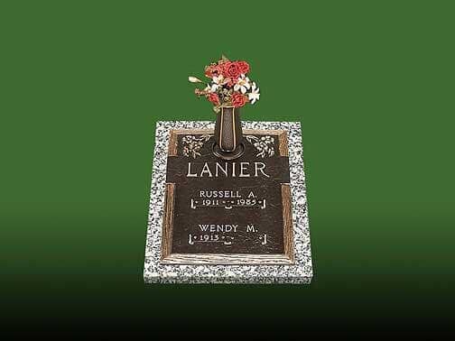 Bronze Lanier headstone with flowers, set in speckled border against a green background.