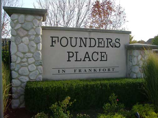 Sign for Founders Place in Frankfort, with stone pillars, green bushes, and a cloudy sky.