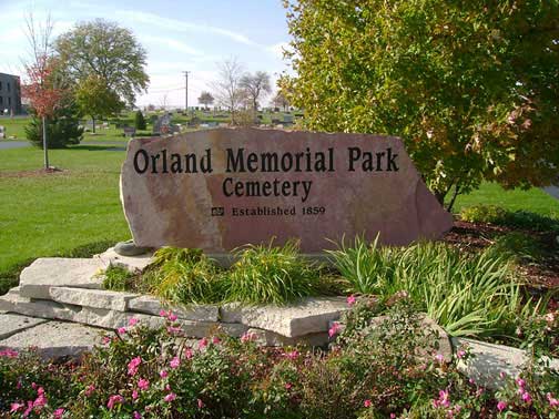Sign for Orland Memorial Park Cemetery established in 1899, surrounded by green grass, plants, and trees.