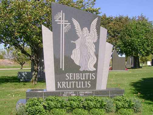 Black granite headstone with an angel, cross, and Lithuanian text in a cemetery.