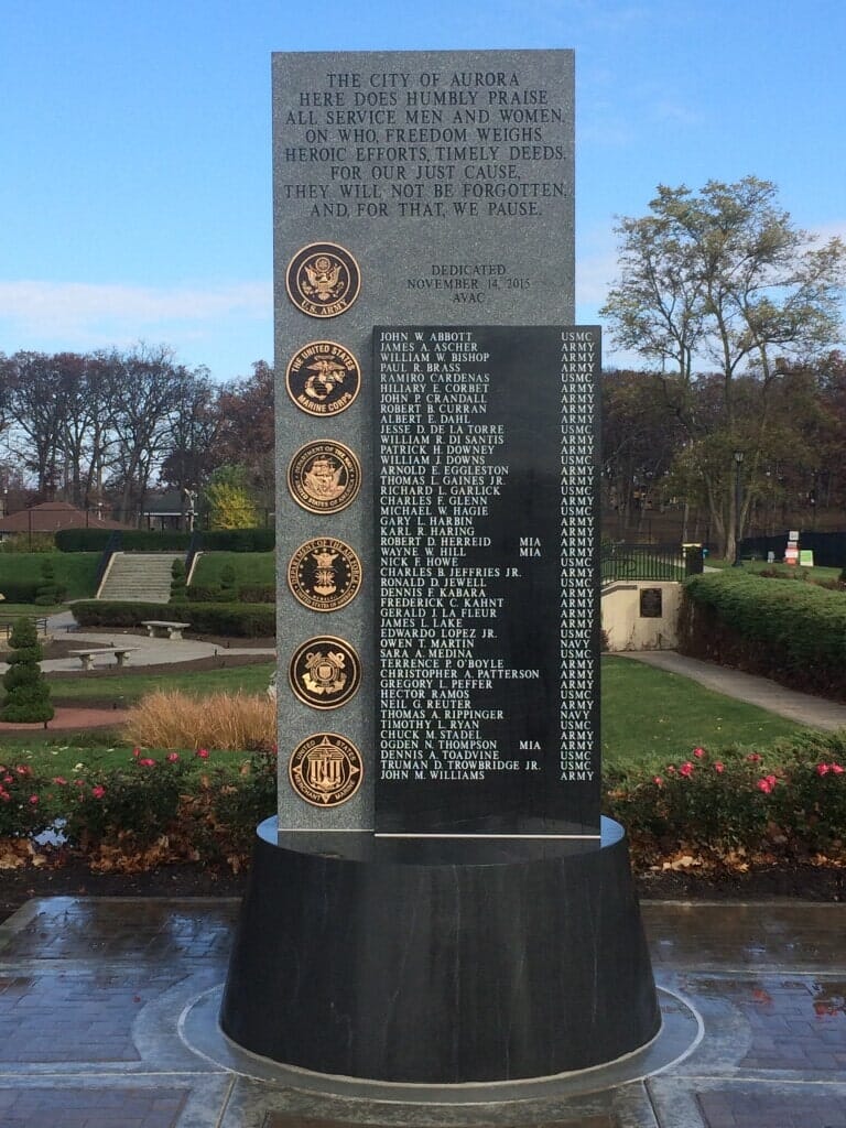 War memorial with names, service seals, and inscriptions in a park setting.
